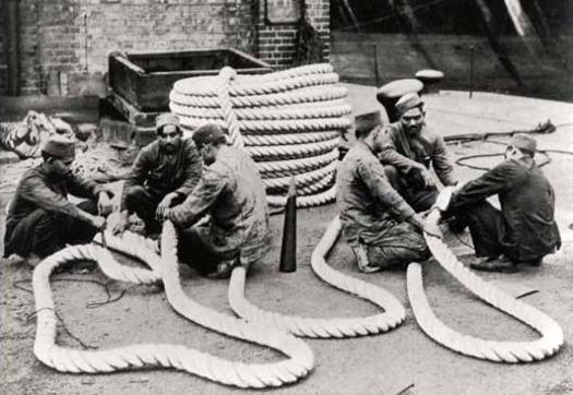 Two groups of three Lascar sailors sit on ground, surrounded by large ropes